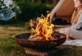 Kampvuur voor een tent met een rustende vrouw bij REBL Outdoor – Bell tenten Friesland glamping.