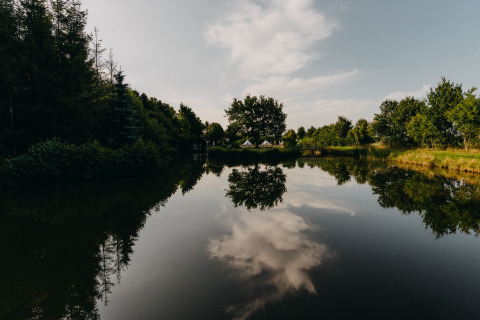 Reflejo de árboles y nubes en un lago en REBL Outdoor – Bell tenten Friesland, alojamiento glamping tranquilo