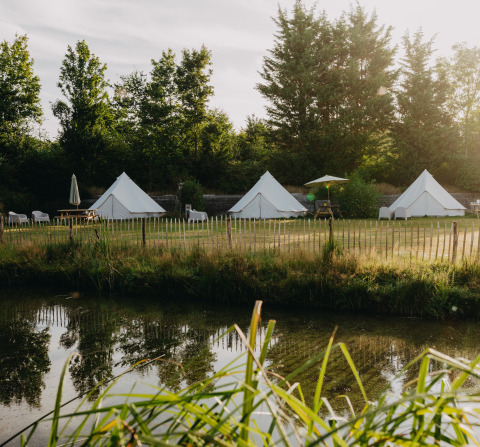 Glamping site with three white bell tents at REBL Outdoor – Bell tenten Friesland near a pond and trees.