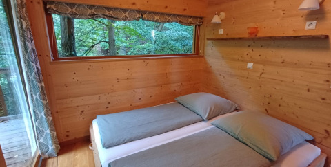 Slaapkamer in Sankt Martin boomhut glamping met houten muren, twee bedden en uitzicht op de natuur.