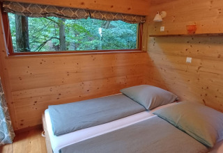 Dormitorio en Sankt Martin boomhut glamping con paredes de madera, dos camas individuales y vista al bosque.