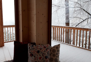 Vista desde Sankt Martin boomhut con cojines en la terraza y árboles cubiertos de nieve en Renania-Palatinado.