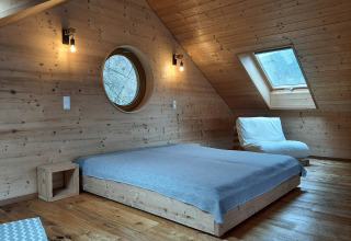 Chambre boisée dans la Sankt Martin boomhut, lit bas, fenêtre ronde et toit incliné, hébergement glamping.