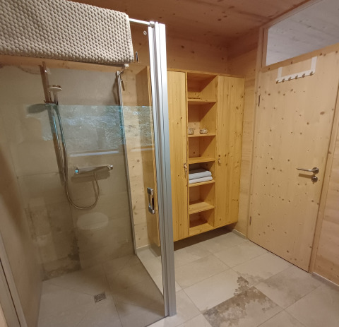 Modernes Bad mit Holzwänden, Dusche, Regal und Tür in einer Glamping-Baumhütte in Sankt Martin.