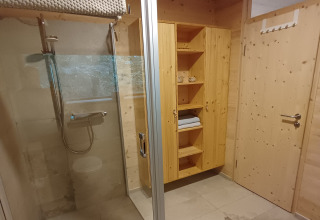 Modernes Bad mit Holzwänden, Dusche, Regal und Tür in einer Glamping-Baumhütte in Sankt Martin.