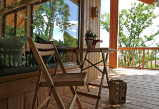 Træhushytte med træveranda, bord og stole, omgivet af natur i glampingindkvartering Sankt Martin.