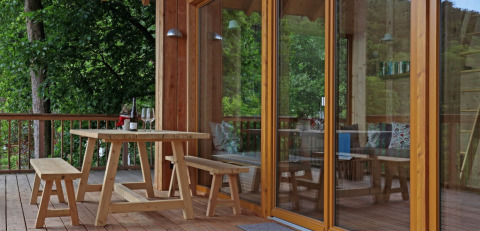Wooden terrace with table and benches by the glass door of glamping hut Sankt Martin, Rheinland-Pfalz, Germany.