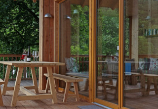 Terrazza in legno con tavolo e panche vicino alla porta a vetri del glamping Sankt Martin boomhut, Renania-Palatinato.