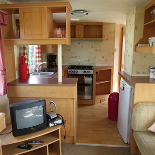 Interno di una casa mobile attrezzata a 'Camping Am Leuchtturm' con cucina e salotto accogliente.