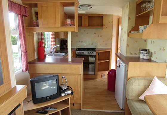 Interno di una casa mobile attrezzata a 'Camping Am Leuchtturm' con cucina e salotto accogliente.