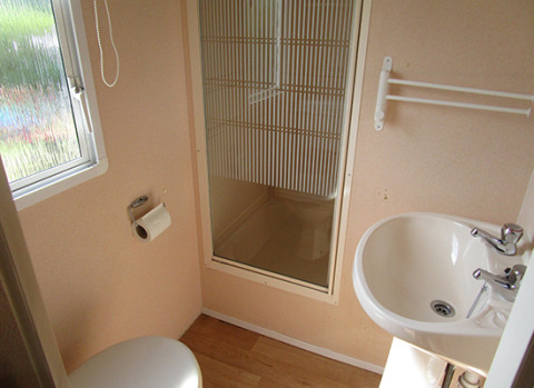 Kompakt badeværelse med toilet, håndvask, bruser og vindue i glamping campingvogn i Niedersachsen.