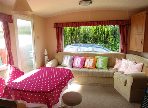 Acogedor interior de glamping con cojines de colores, sofá grande y mantel de lunares rojos.