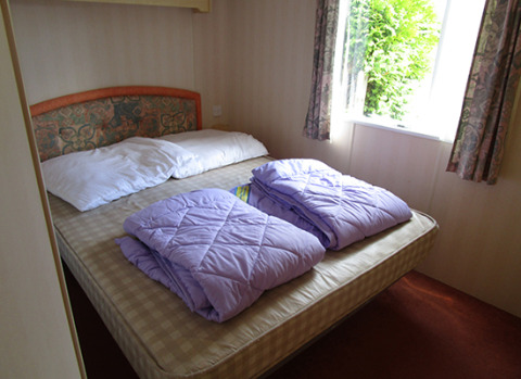 Slaapkamer in een glamping stacaravan op Camping 'Am Leuchtturm' met dubbelbed en lila dekbedden.