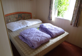 Chambre dans un mobil-home glamping au Camping 'Am Leuchtturm' avec lit double et couettes lilas.