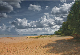 Zandstrand met groen en wolkenluchten bij Camping Am Leuchtturm glamping in Nedersaksen.