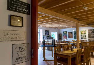 Sala da pranzo accogliente con tavoli in legno e citazioni sulle pareti presso Natuurcamping Lassan.