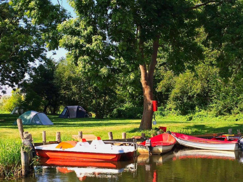 Camping Natuurcamping Lassan - Wijnvaten Mecklenburg-Vorpommern, tiendas y barcos cerca de un lago tranquilo.