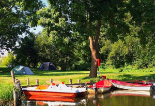 Natuurcamping Lassan - Wijnvaten Mecklenburg-Vorpommern, tenten en boten bij bomen aan een rustige meerzijde camping.