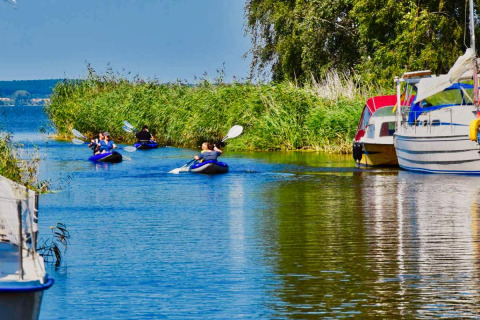 Personas remando en kayak por un canal en Natuurcamping Lassan, con barcos y juncos en Mecklenburg-Vorpommern.