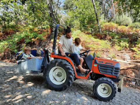 Un hombre y niños en un pequeño tractor en un entorno forestal en Land of Deveza - Glamping Portugal, aventura en la naturaleza.