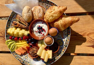 Vassoio colazione colorato con frutta, pane, croissant, uova e yogurt a Land of Deveza Glamping Portogallo.