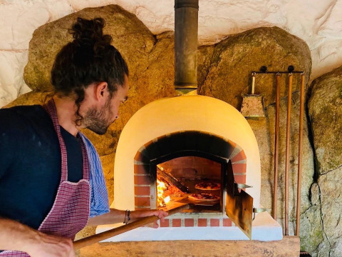 Een man bakt pizza's in een traditionele steenoven bij Land of Deveza - Glamping Portugal, gezellige glamping.