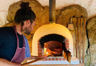 Ein Mann backt Pizza in einem traditionellen Steinofen bei Land of Deveza - Glamping Portugal Campingplatz.