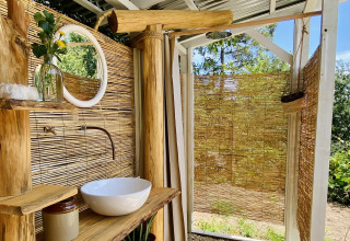 Salle de bain extérieure en bois et bambou, lavabo et miroir chez Land of Deveza Glamping Portugal.