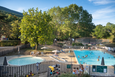 Families relax by the pool surrounded by trees at Huttopia Divonne Les Bains glamping in Rhône-Alpes.