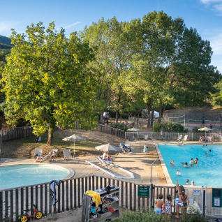 Families relax by the pool surrounded by trees at Huttopia Divonne Les Bains glamping in Rhône-Alpes.