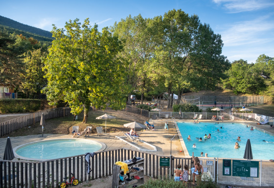 Families relax by the pool surrounded by trees at Huttopia Divonne Les Bains glamping in Rhône-Alpes.