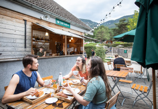 Tre personer nyder morgenmad på udendørs café ved Huttopia Divonne Les Bains - Glamping Rhône-Alpes.