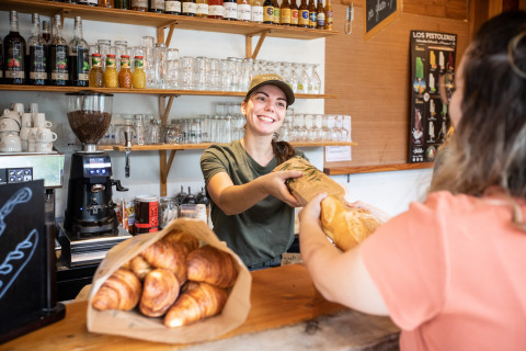 Una commessa sorridente consegna del pane fresco a una cliente in una panetteria accogliente e ben fornita.