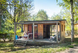 Cabane en bois moderne à Huttopia Divonne Les Bains Glamping Rhône-Alpes, avec des invités relaxant sur la terrasse.