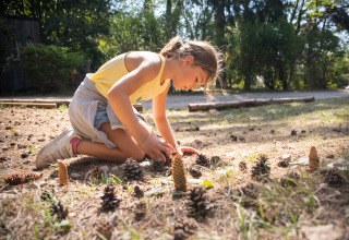 A child playing with pinecones outdoors at Huttopia Divonne Les Bains - Glamping Rhône-Alpes campsite.