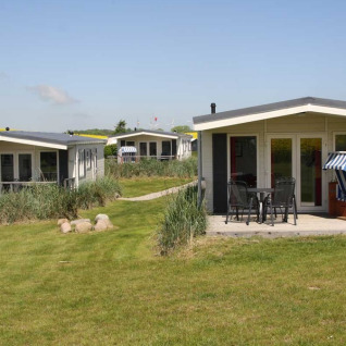 Tre moderni lodge glamping al Camping Walkyria sull’Ostsee, con terrazza, sedie e tanto verde.