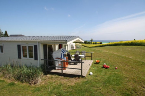 Alloggio glamping a Camping Walkyria con terrazza, vista mare, sedie da giardino e giocattoli sul prato.