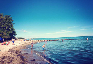 Beach scene at Camping Walkyria - Lodges aan de Oostzee with people swimming and relaxing by the shore.
