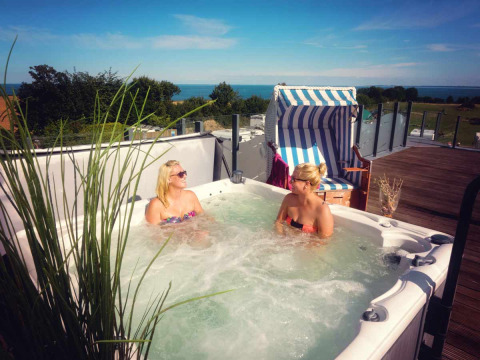 Twee vrouwen relaxen in een bubbelbad op een terras met zeezicht bij Camping Walkyria - Lodges aan de Oostzee.