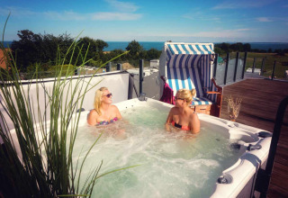 Two women relaxing in an outdoor hot tub on a terrace with sea view at Camping Walkyria - Lodges aan de Oostzee.