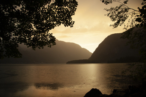 Tramonto sul lago e sulle montagne vicino a Park am See, glamping a Obertraun, Austria, tra rami d'albero.