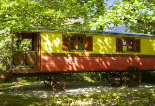 Colorful wooden wagon under lush green trees, glamping accommodation at Park am See, Obertraun, Austria, summer vibe.