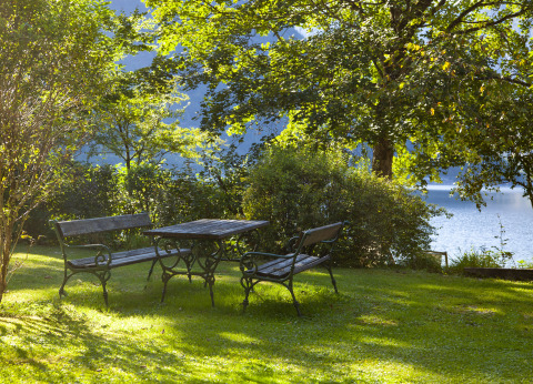 Área de descanso al aire libre con bancos y mesa de madera en jardín verde junto al lago en Park am See, Obertraun