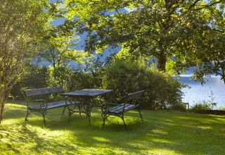 Outdoor seating with wooden benches and table in green garden by the lake at Park am See, Obertraun, Austria