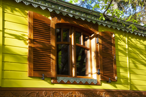 Bunte Holzfassade mit grüner Wand und offenen Fensterläden bei Park am See Glamping in Obertraun, Österreich.