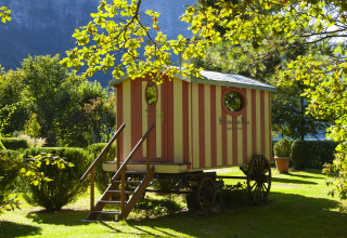 Glamping-Unterkunft: rot-gelber Wagen im Park am See, Ferienhaus in Obertraun, Österreich, Garten.