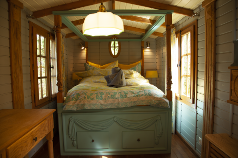 Alojamiento glamping acogedor con cama con dosel, ventanas de madera y luz cálida en Obertraun, Austria.