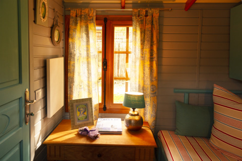 Hébergement glamping douillet avec lumière du soleil à travers les rideaux, bureau et coussins rayés.