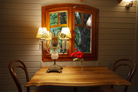 Acogedora zona de comedor con mesa de madera, dos sillas, lámpara antigua y flores rojas junto a ventana.