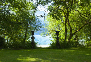 Lush green park by the lake with trees and urns, Park am See glamping accommodation in Obertraun, Austria.